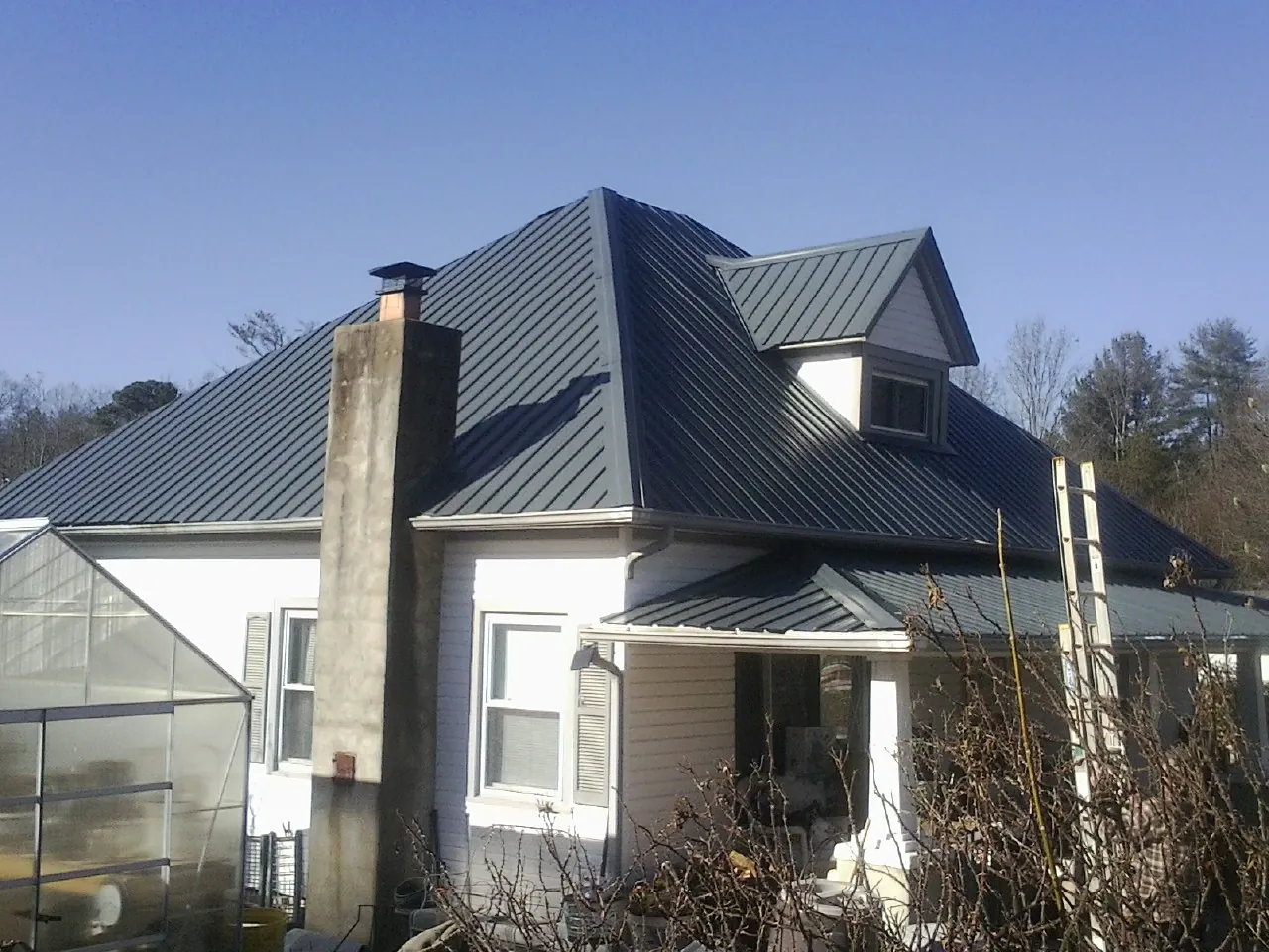 Dark blue standing seam metal roof on a white farmhouse with dormer — Slate & Tile Roof Repair by Roofing Brothers in Mcchord Afb