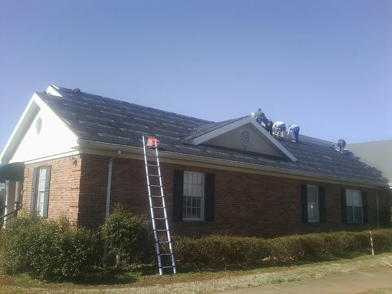 Crew tearing shingles off a brick ranch roof with a ladder set — Emergency Roof Repair work by our crew in Mcchord Afb