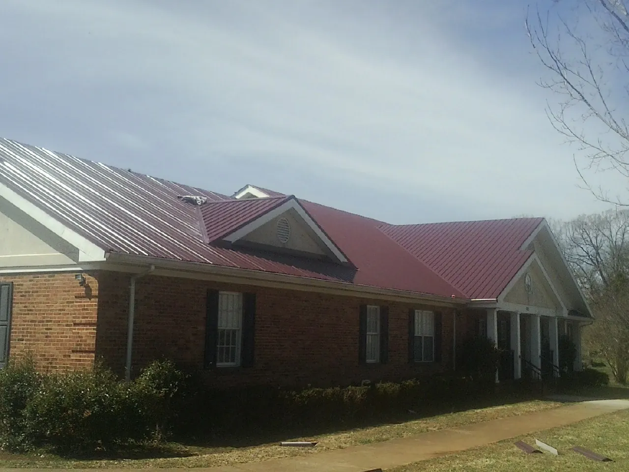 Red metal roof with gabled entries on a long brick building, from a Hail Damage Roof Repair job in Mcchord Afb