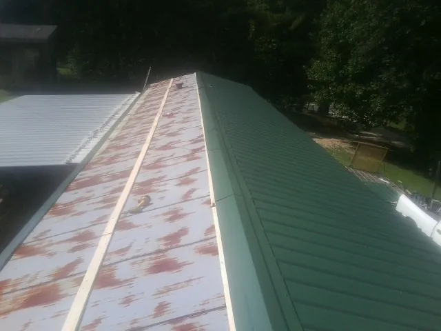 Old rusted panels beside newly installed green metal roofing — Wind Damage Roof Repair by Roofing Brothers in Mcchord Afb