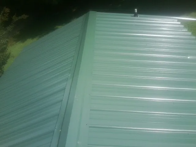 New green metal panels meeting at the ridge of a roof — Flat Roof Repair work by our crew in Mcchord Afb