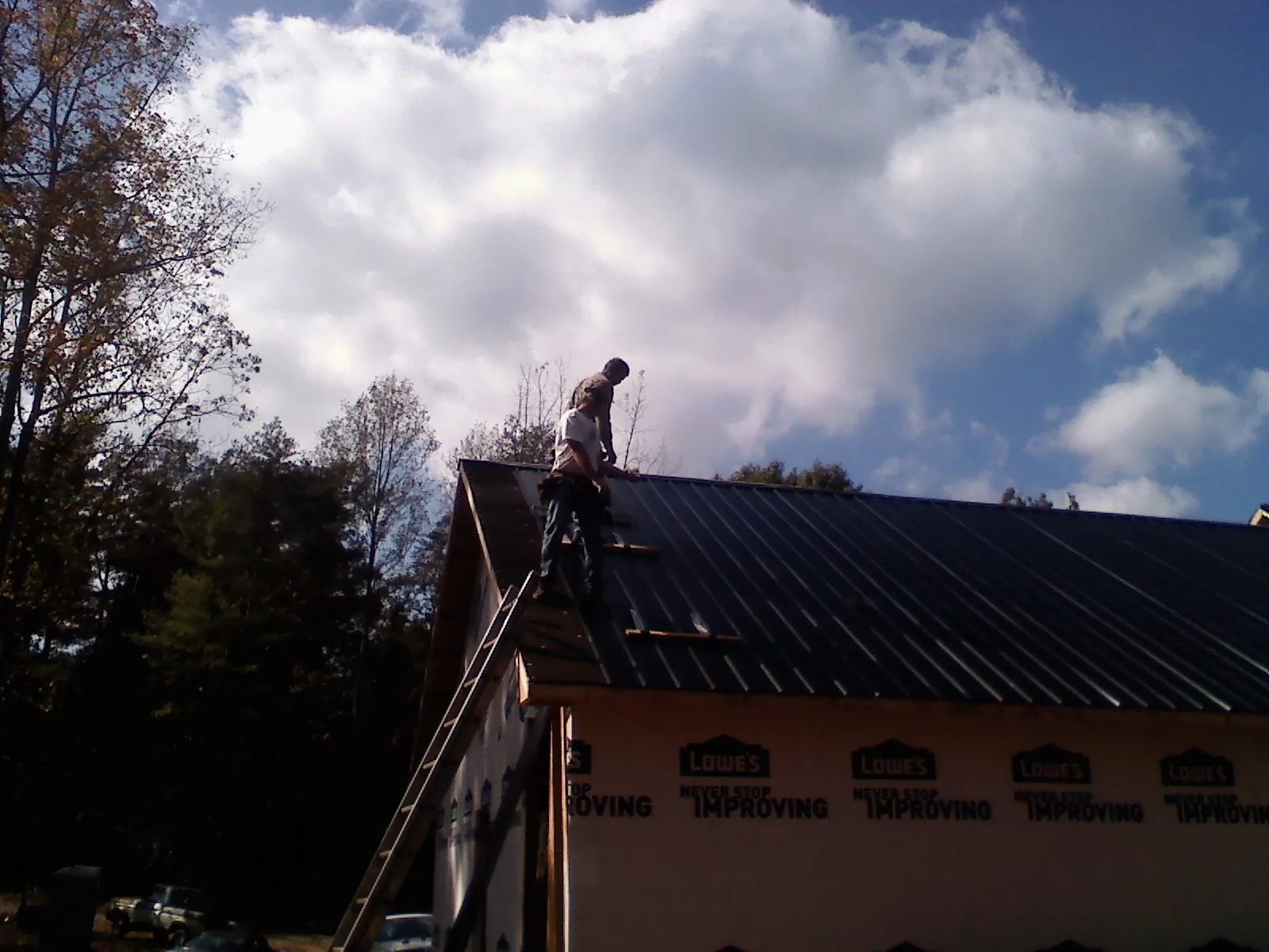 Roofer fastening dark metal panels high against a cloudy sky, from a Roof Inspection job in Mcchord Afb