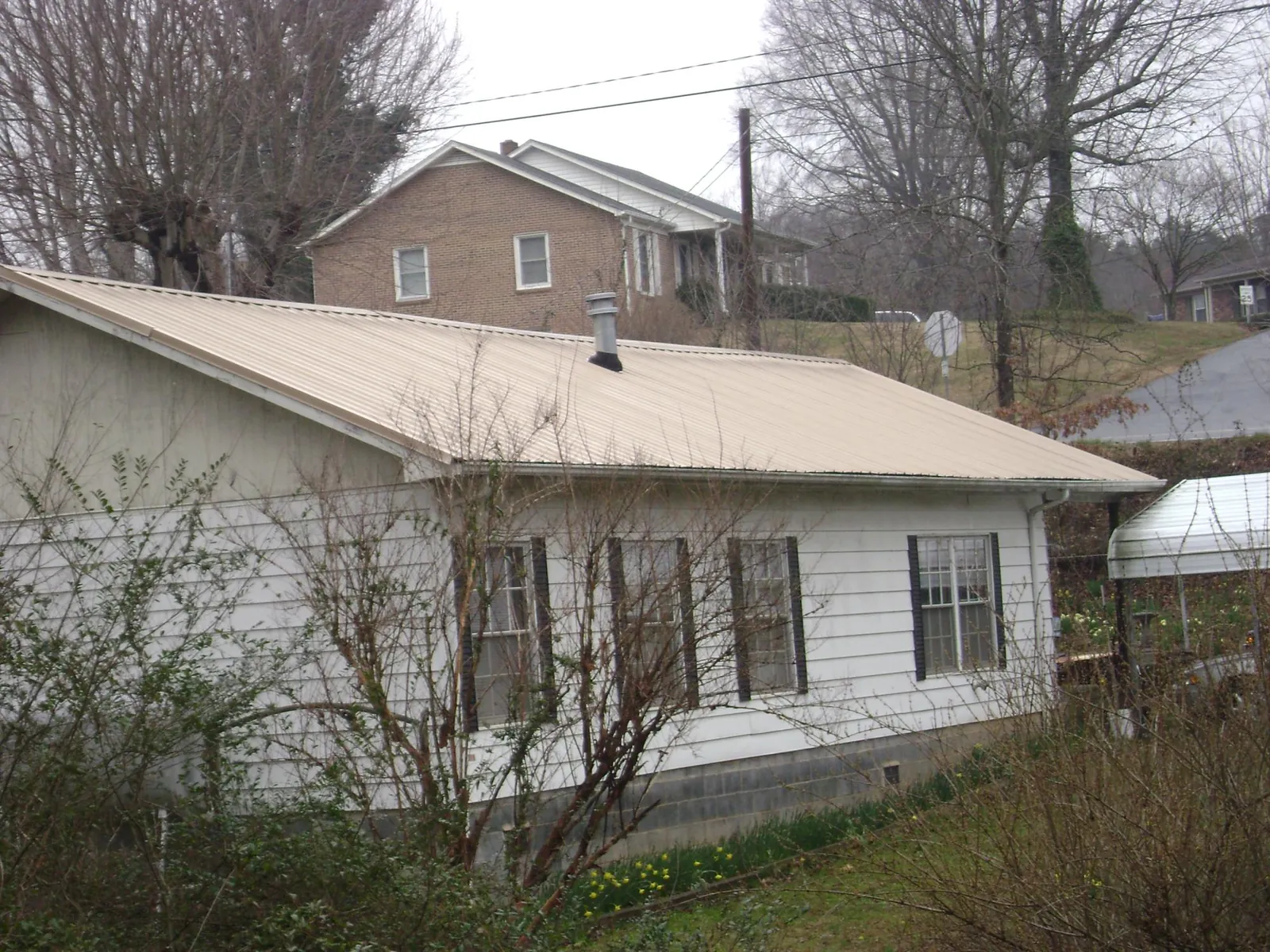 Tan metal roof on a white sided house set into a hillside — Commercial Roofing by Roofing Brothers in Mcchord Afb